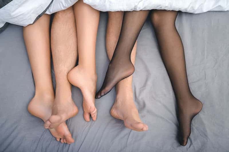 drei Beinpaare im Bett unter einem weißen Laken