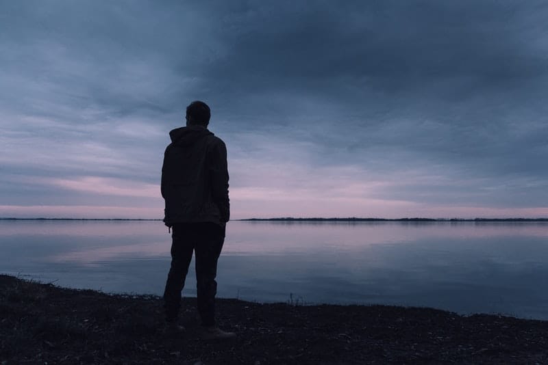 ein Mann, der allein in der Dämmerung am Strand steht