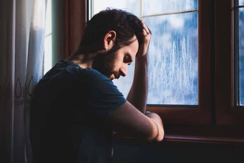 trauriger Mann, der seinen Kopf vor Fenster hält