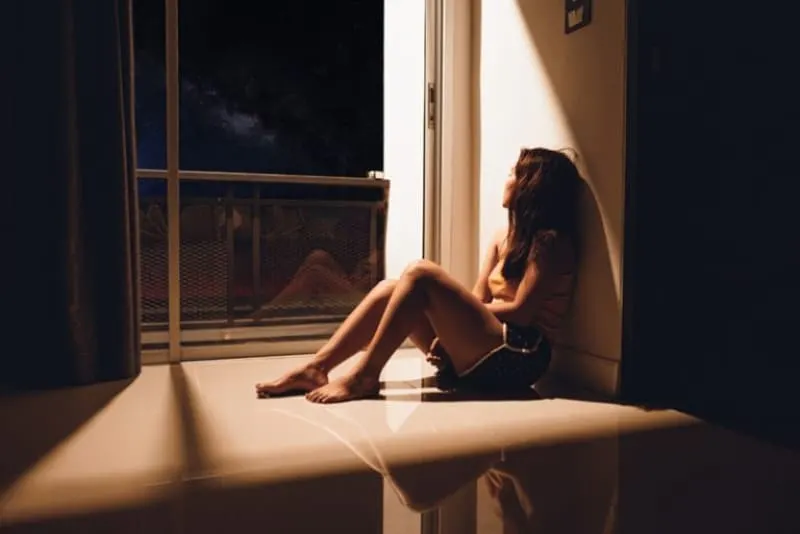 ein einsames Mädchen, das im Mondlicht am Fenster am Boden sitzt