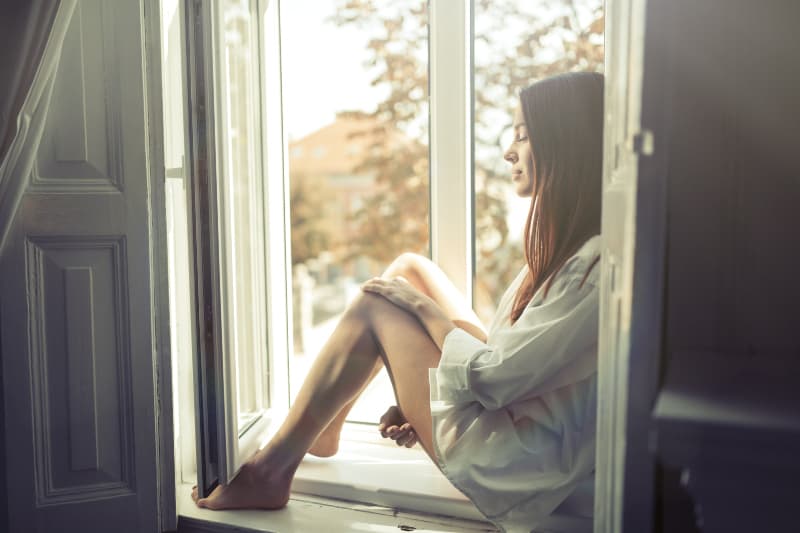 Ein Mädchen in einem weißen Hemd sitzt auf einem Fensterbrett