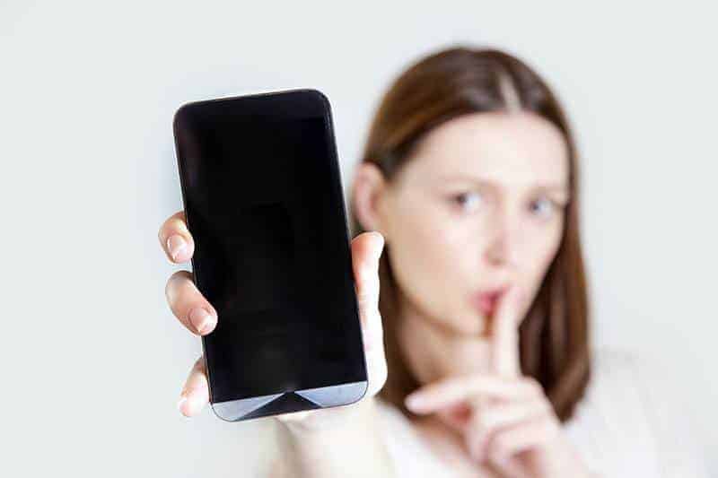 Frau, die Telefon hält, während sie Schweigenzeichen mit Finger gestikuliert
