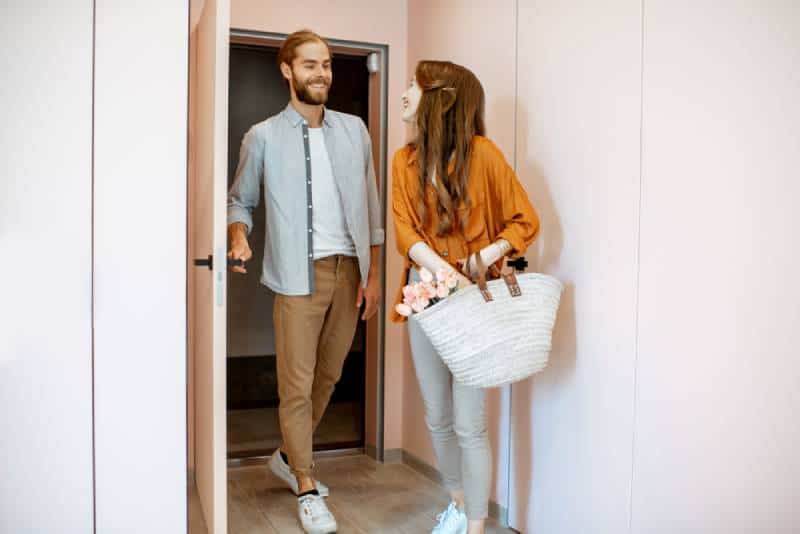 Schönes junges Paar, das nach Hause kommt und zusammen im rosa Korridor der modernen Wohnung geht