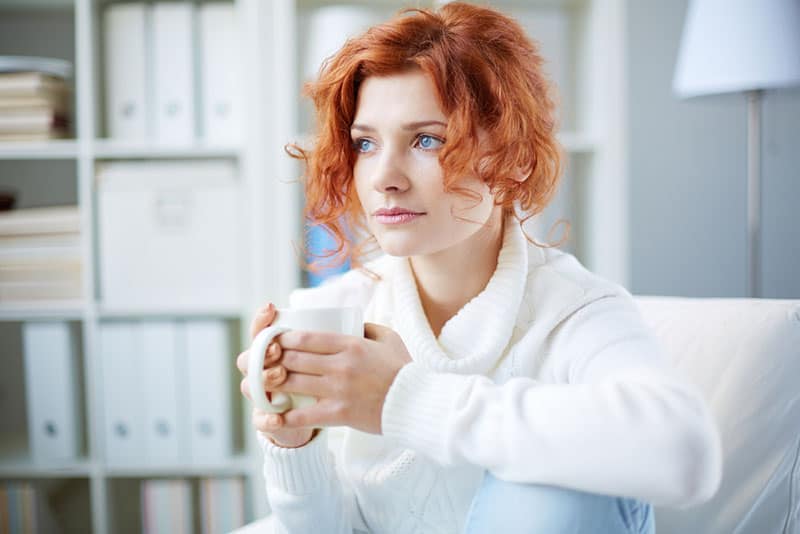 schöne Frau mit roten Haaren und blauen Augen, die Kaffee trinken