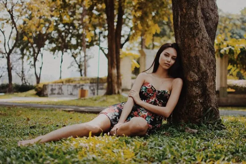 Ein einsames Mädchen sitzt im Gras und lehnt sich an einen Baum