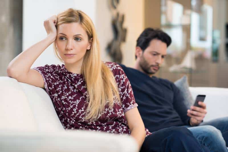 Junge Frau, die sich langweilt, während Mann Telefon benutzt