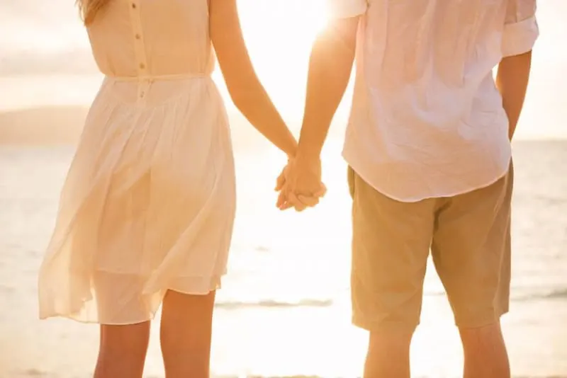 ein Paar, das Händchen haltend am Strand entlang geht