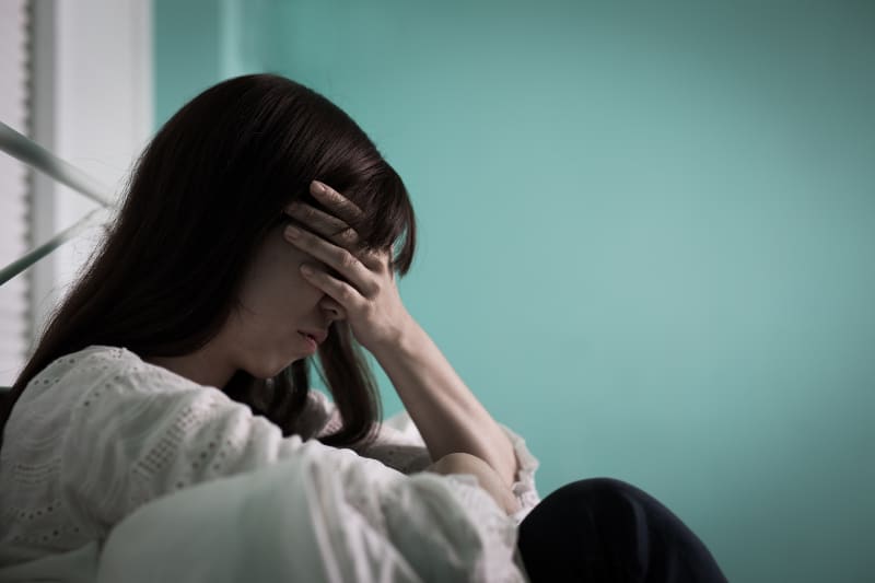 eine Frau, die sich deprimiert fühlt und auf dem Bett sitzt