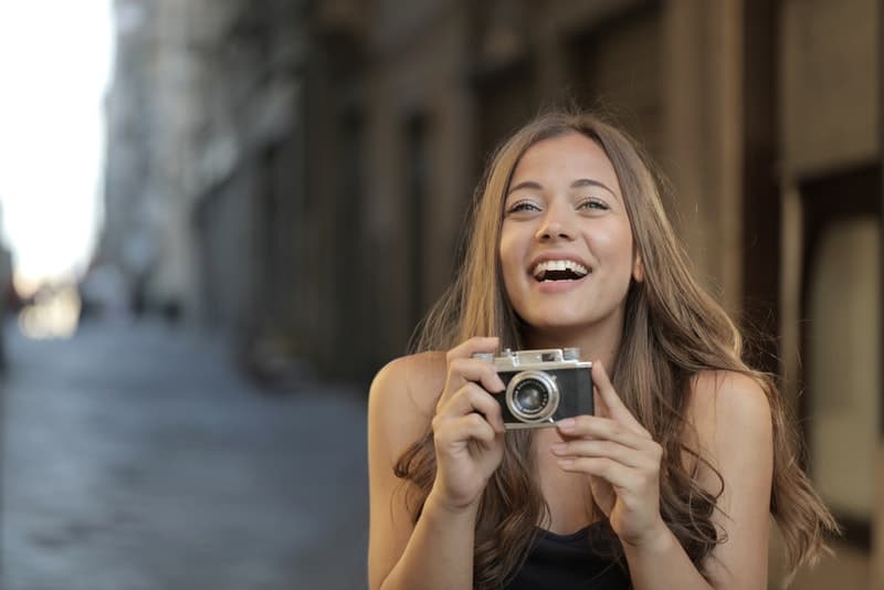 Auf der Straße steht eine lächelnde Frau mit einer Kamera in der Hand