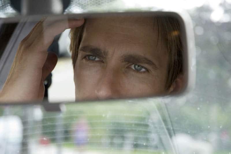Der Mann sitzt im Auto und schaut in den Rückspiegel