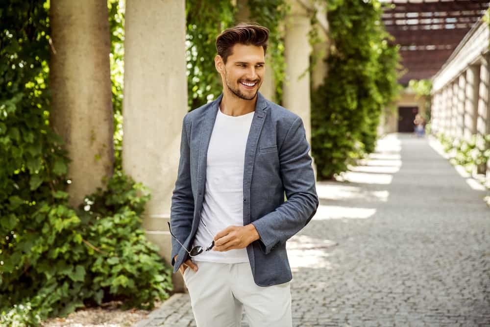 Draußen steht ein lächelnder Mann in grauer Jacke und weißer Hose