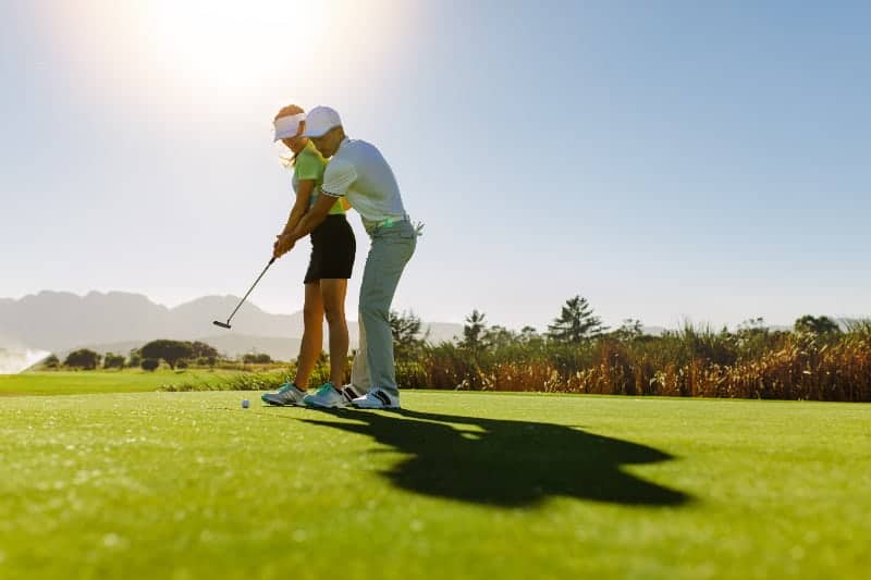 Ein Mann bringt einer Frau das Golfspielen bei