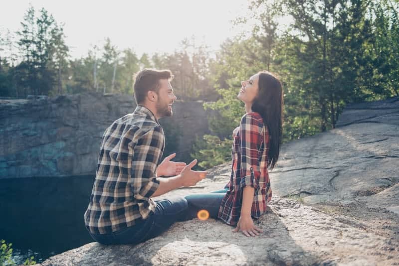 Ein Mann erzählt seiner Frau etwas Lustiges, während er auf einem Felsen in der Natur sitzt