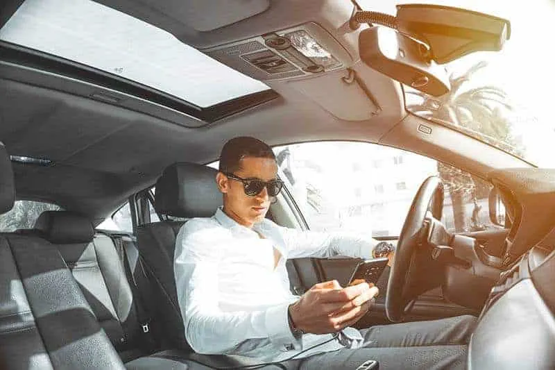 Ein Mann mit Sonnenbrille im Auto benutzt ein Handy