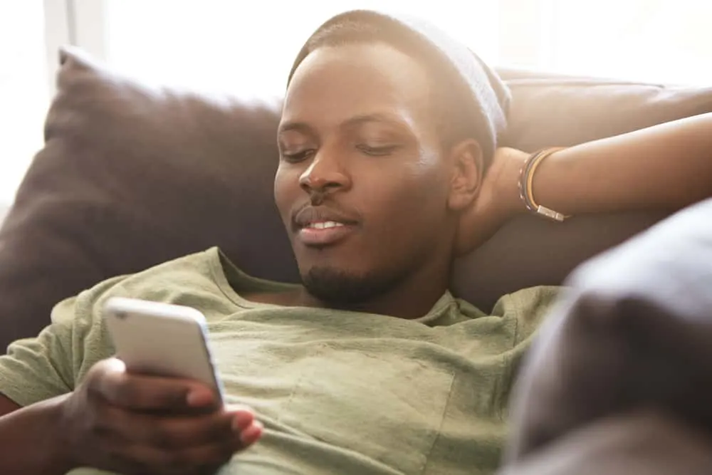 Ein junger schwarzer Mann liegt auf der Couch und benutzt ein Handy