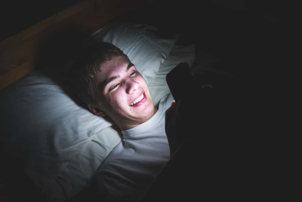 Ein lächelnder Mann liegt im Bett und schreibt eine SMS
