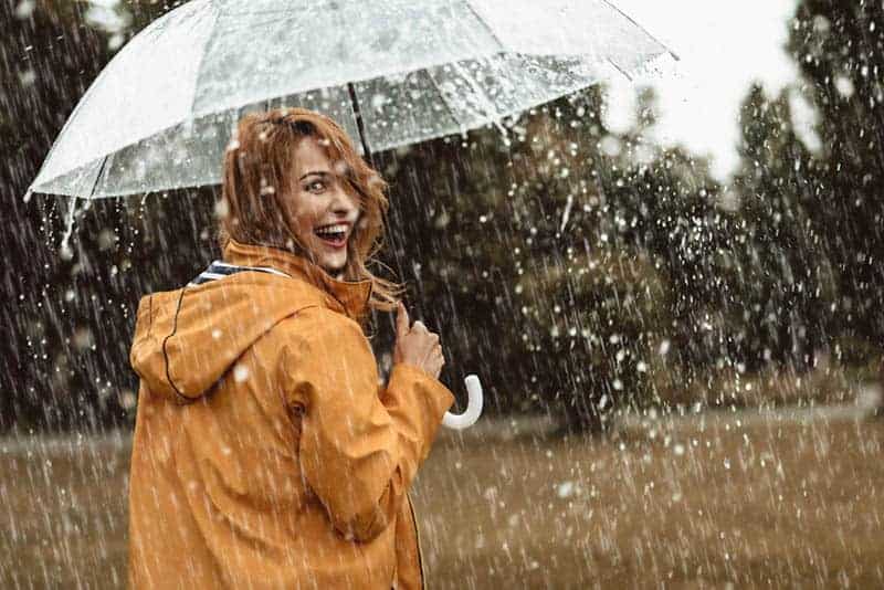 Ein lächelndes Mädchen mit einem durchsichtigen Regenschirm geht im Regen