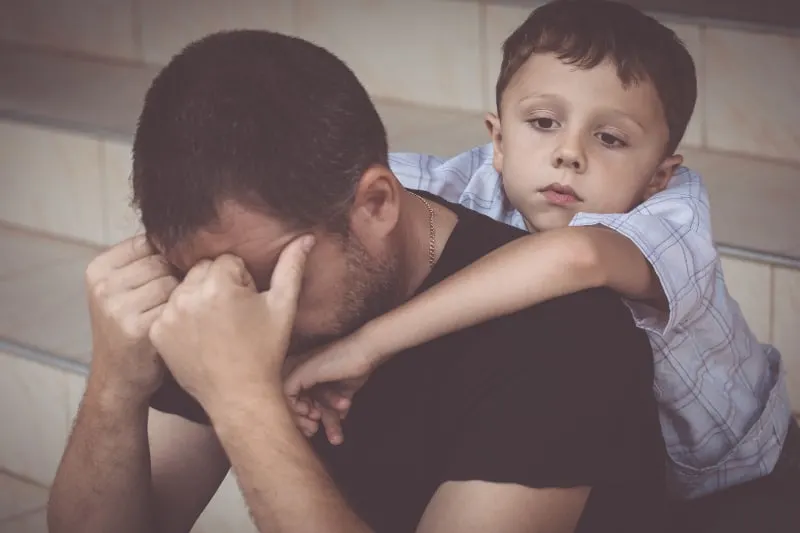 Ein trauriger Junge umarmt seinen desinteressierten Vater