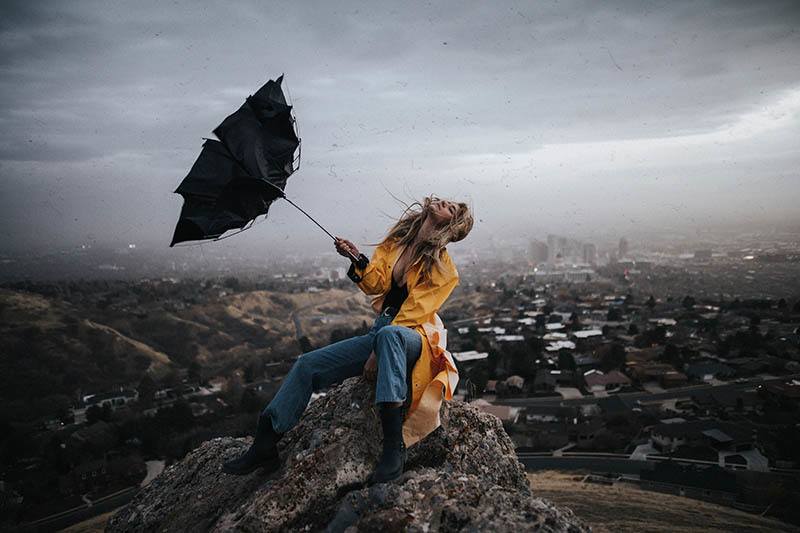Eine Frau in einem gelben Regenmantel mit einem kaputten Regenschirm genießt den Sturm