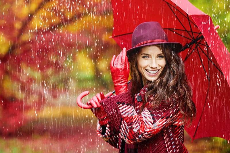 Eine lächelnde Frau mit roten Handschuhen und einem roten Regenschirm steht im Regen