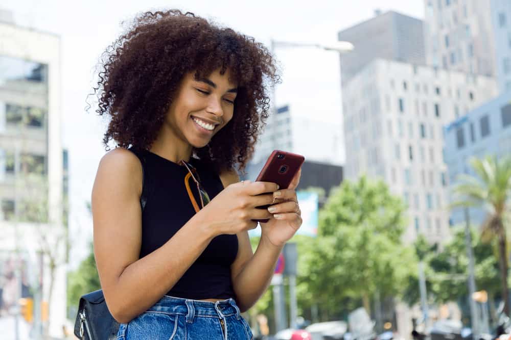 Eine schöne junge schwarze Frau mit einem Lächeln benutzt ein Handy