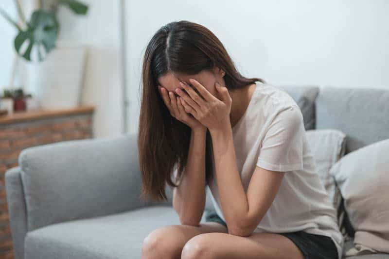 Eine traurige Frau sitzt auf der Couch und hält ihr Gesicht mit den Händen fest