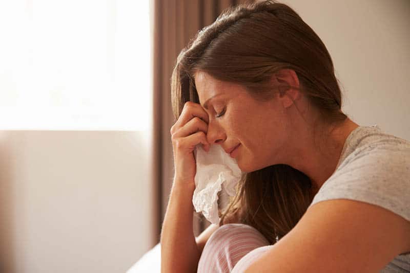 Eine weinende Frau sitzt und hält ein Taschentuch in der Hand