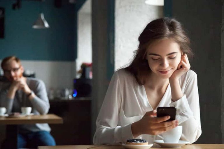 eine lächelnde Frau, die in einem Café sitzt und ein Handy benutzt