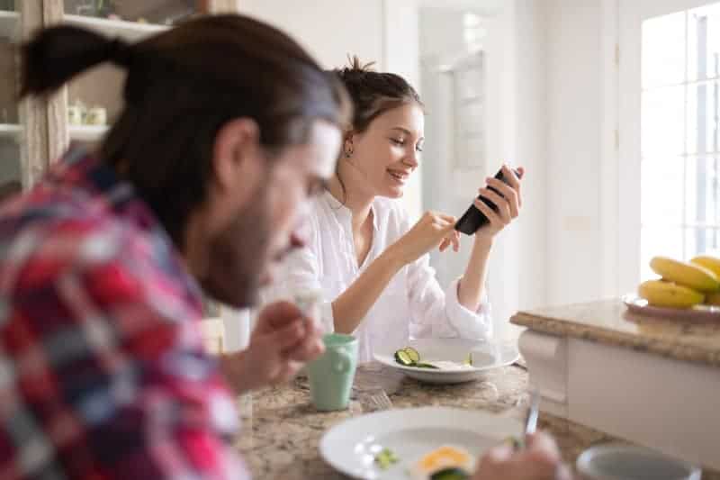 Frühstück eines Mannes und einer Frau, die unterwegs auf ein Handy schauen und lachen