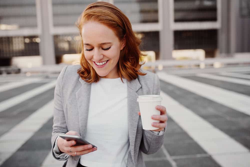 Porträt einer lächelnden Geschäftsfrau mit einem Telefon und Kaffee in ihren Händen