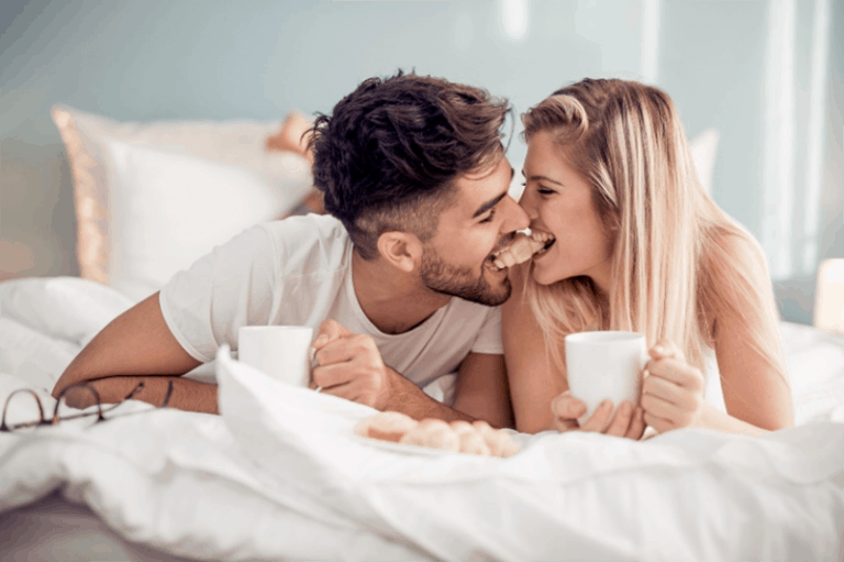 Ein Paar liegt auf dem Bett und trinkt Kaffee
