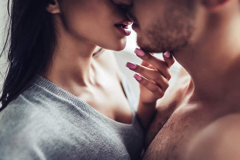 Eine Frau mit rosa Nagellack hält einen Mann am Kinn und küsst ihn leidenschaftlich