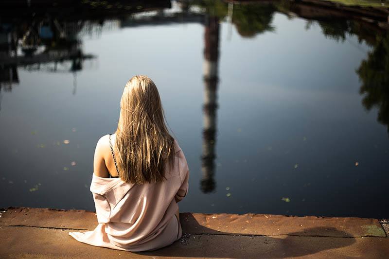 Rückansicht der blonden Frau, die auf hölzernem Dock vor See sitzt