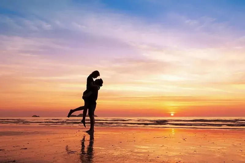 Mann haelt Frau im Arm bei Sonnenuntergang