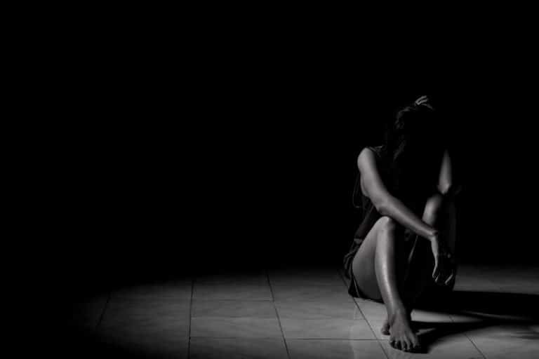 ein depressives Mädchen, das im Dunkeln auf den Fliesen sitzt