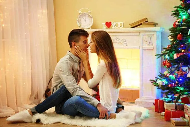 ein glückliches Liebespaar, das während der Weihnachtsferien auf dem Boden des Raumes sitzt und sich küsst