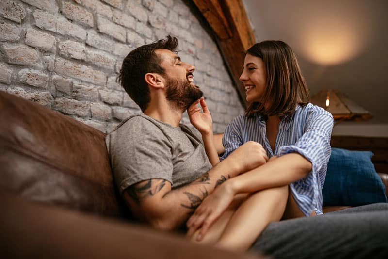 glückliche Frau, die auf Mann im Wohnzimmer sitzt