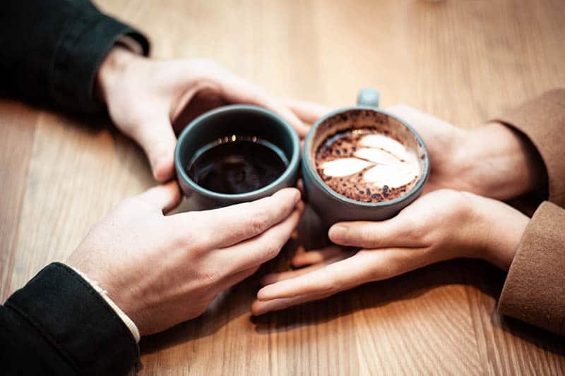 männliche und weibliche Hände halten zwei Tassen Kaffee auf dem Tisch