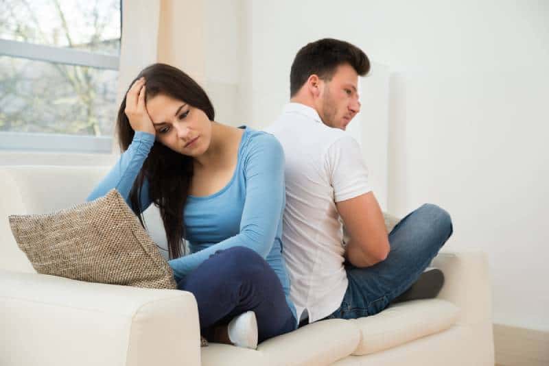 nachdenkliches Paar, das Rücken an Rücken auf der Couch sitzt