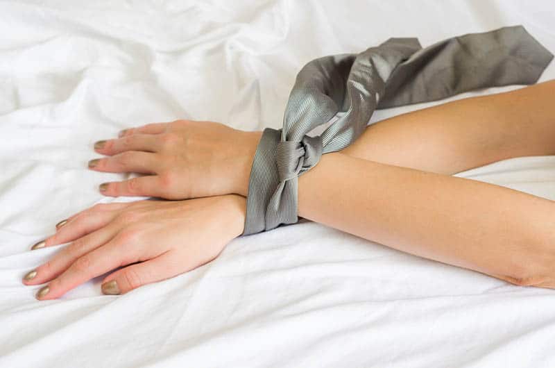 weibliche Hände mit einer Krawatte auf dem Bett gebunden