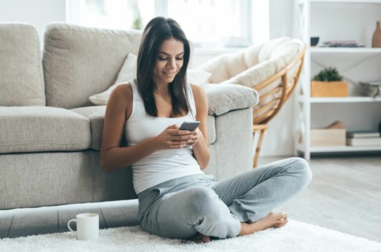 junge Frau sitzt auf dem Boden und schreibt eine SMS