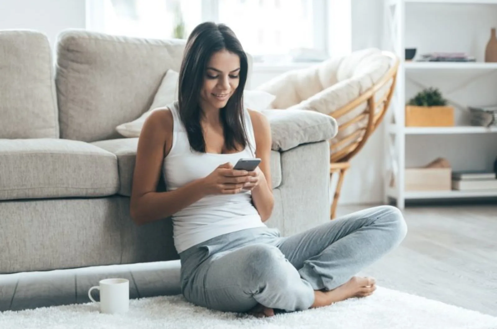 junge Frau sitzt auf dem Boden und schreibt eine SMS