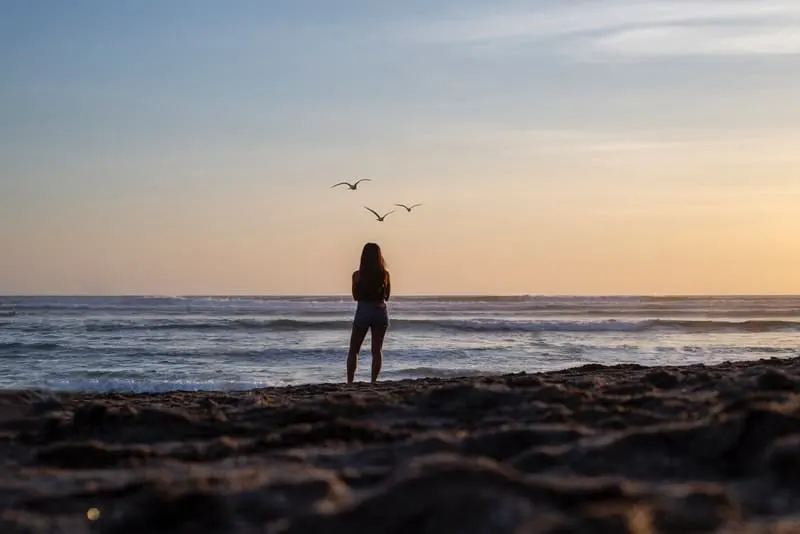 Am Strand am Meer steht eine Frau in kurzen Hosen