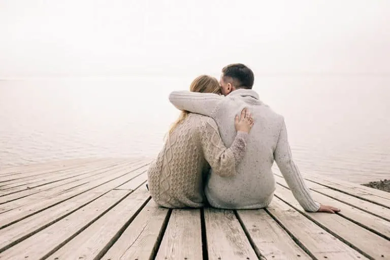 Das umarmende Paar sitzt auf den Brettern am See