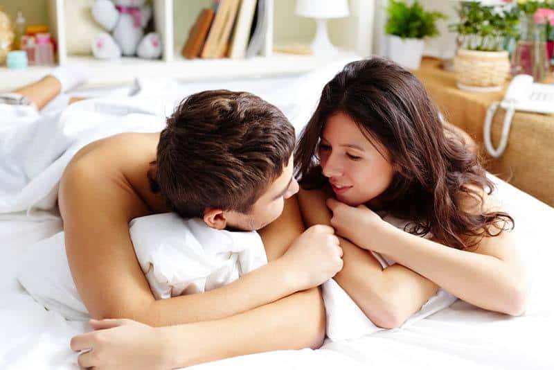 Die Brünette und ihr Mann liegen zufrieden unter einem weißen Laken im Bett