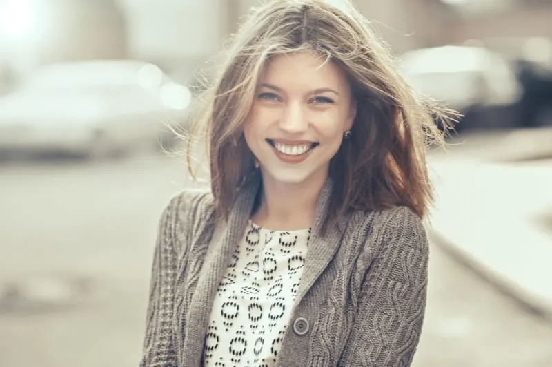 Draußen steht ein schönes lächelndes Mädchen in einem Pullover