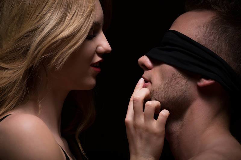 Ein Mann mit verbundenen Augen, dessen Lippen von einer sexy Frau berührt werden