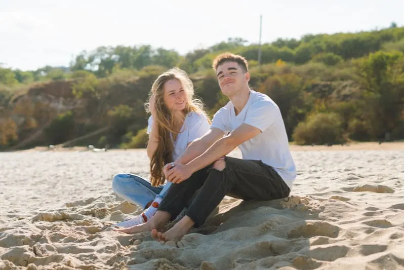 Ein lächelndes junges Liebespaar sitzt an einem Sandstrand