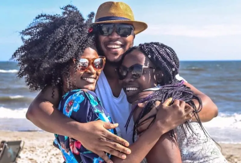 Ein-schwarzer-Mann-am-Strand-umarmt-zwei-schwarze-Frauen