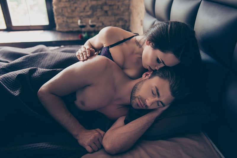 Eine Frau flüstert einem Mann ein Ohr zu, während sie auf dem Bett liegen
